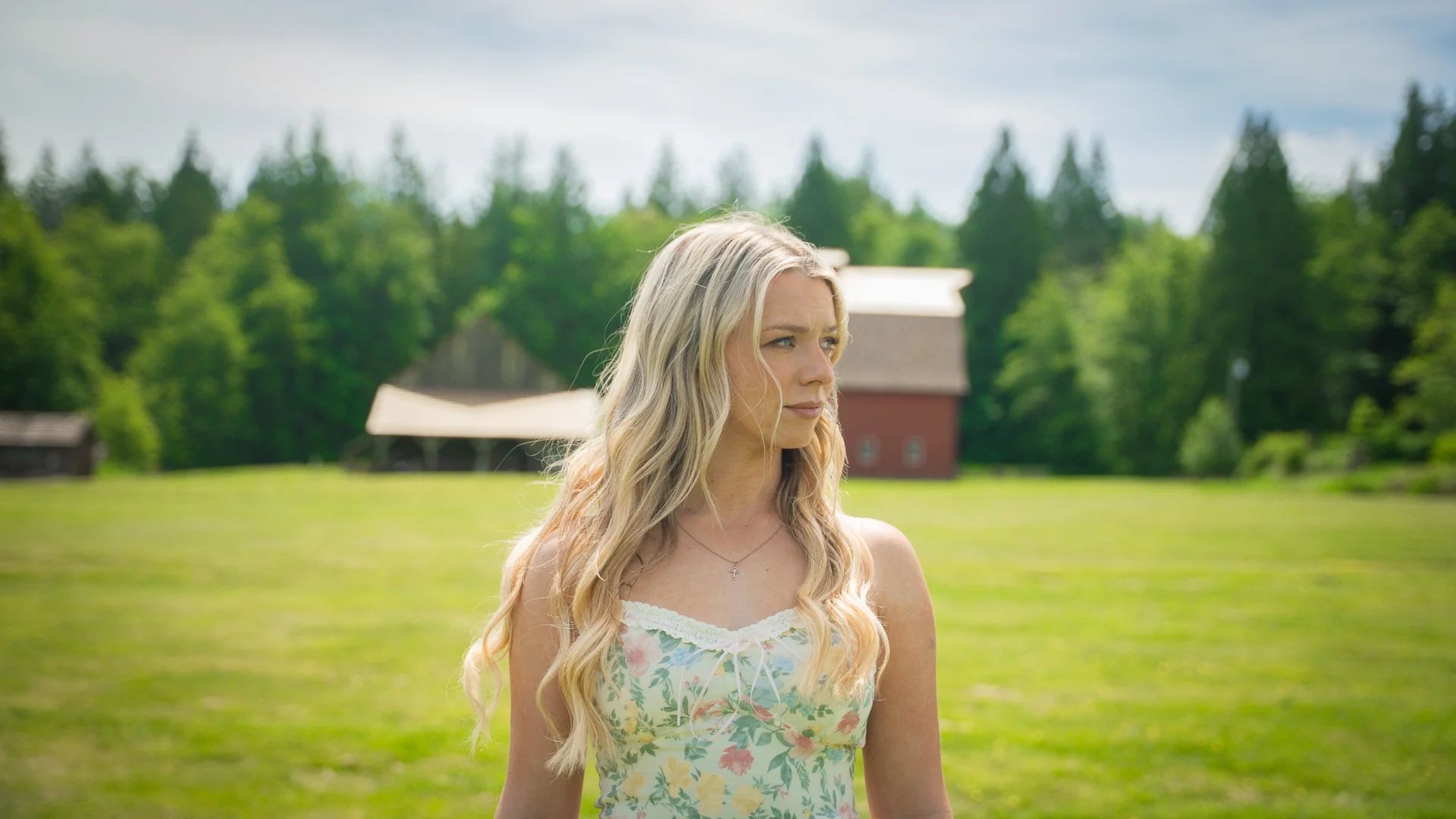 Emily Nelson in a sunlit field with a red barn behind her